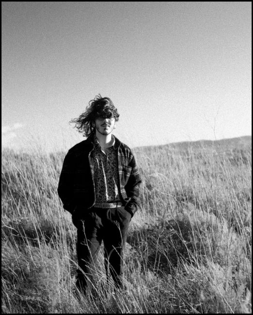 Black and white portrait of a young man standing in a windy field.