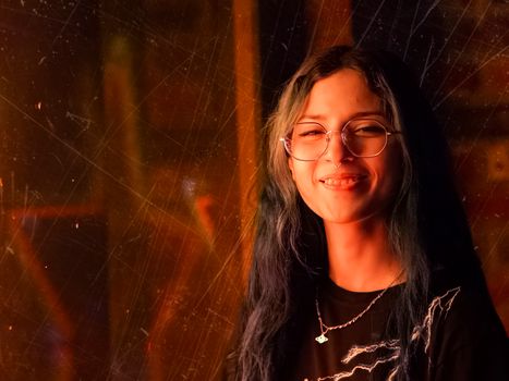 A cheerful young woman with glasses smiling, illuminated by warm light and artistic shadows.