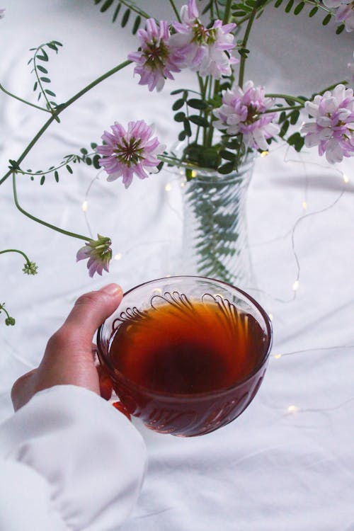 Woman Holding Cup of Tea near Blooming Flowers