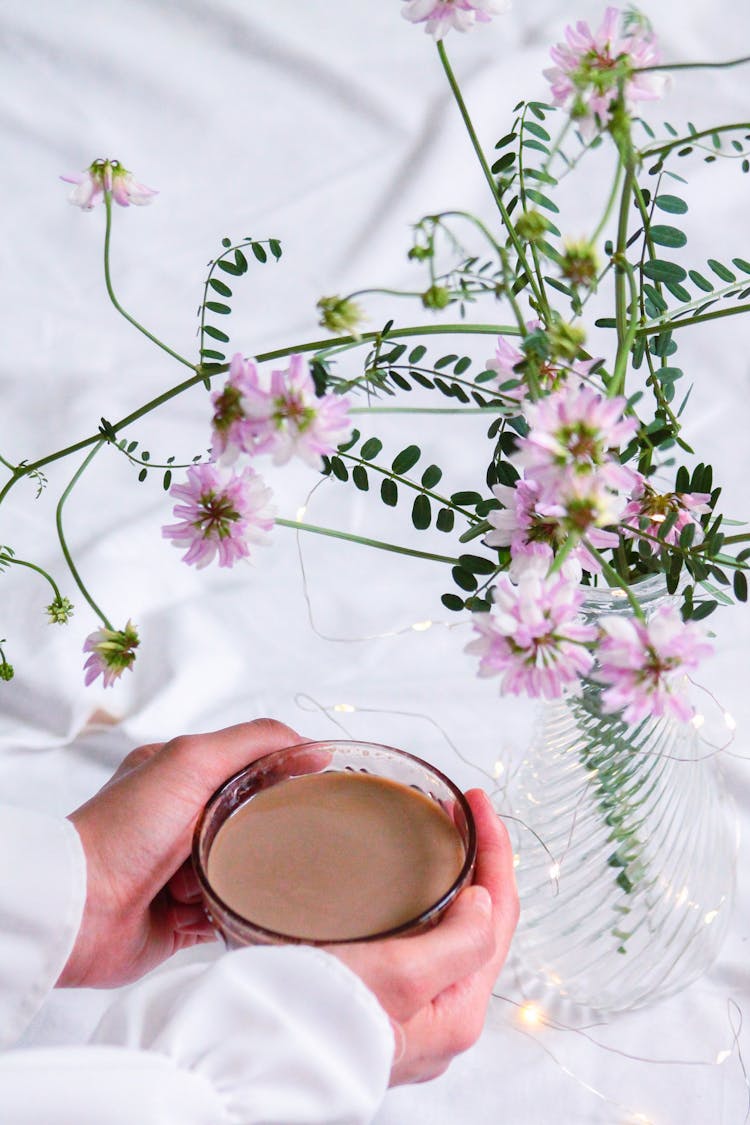 Woman Holding Cup Of Coffee Near Flowers Bouquet