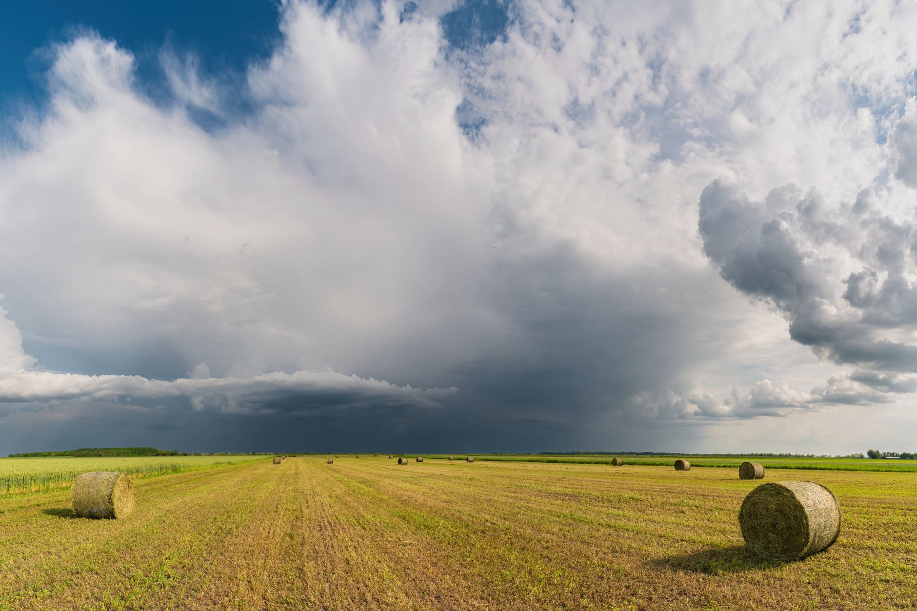 Explore the vast rural landscape with hay bales under a dynamic summer sky. Perfect for nature lovers.