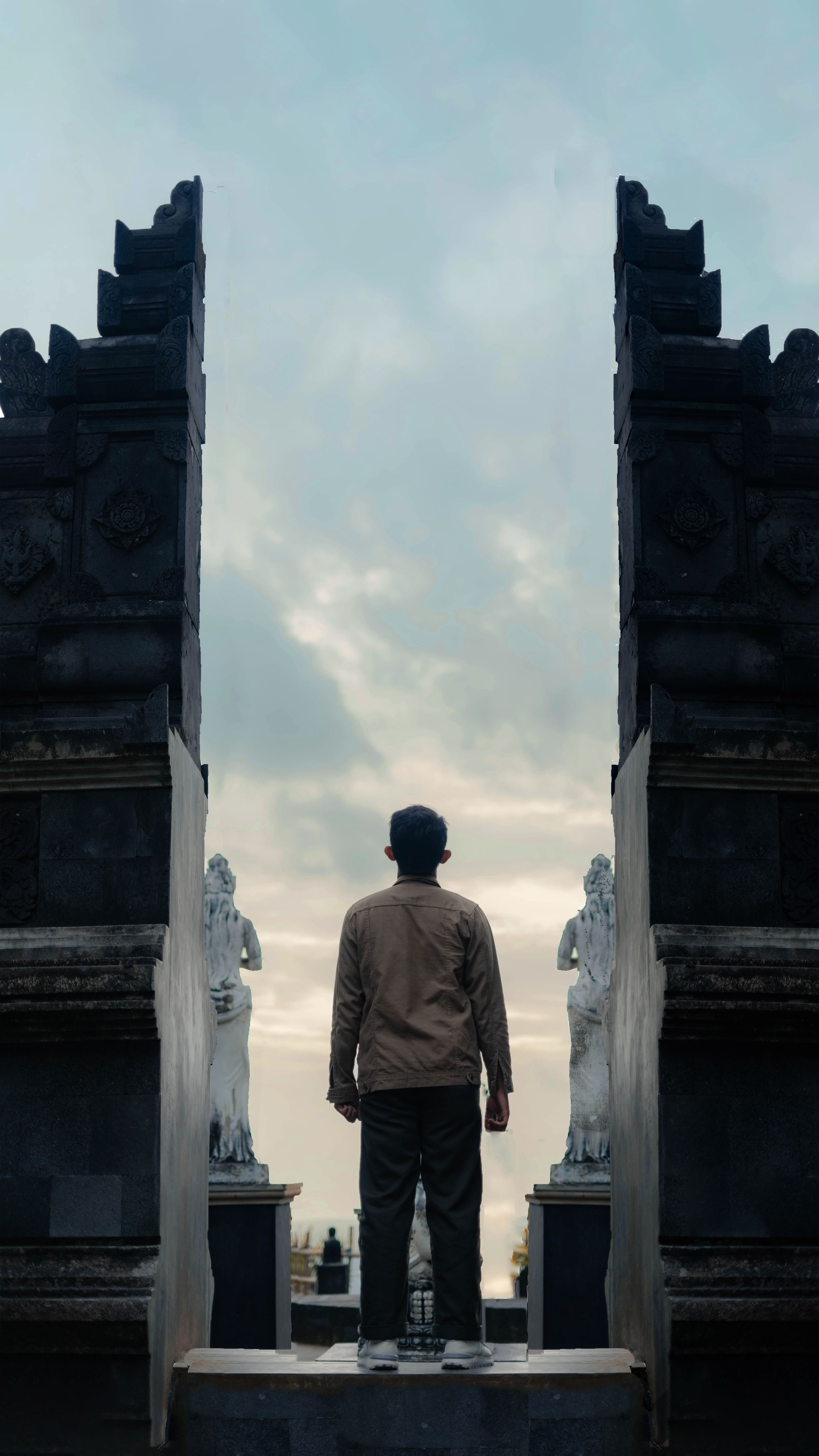 A man stands with his back to the camera, gazing at an ancient temple entrance, symbolizing contemplation and solitude.