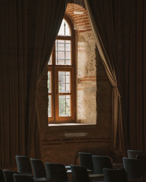 Free A dimly lit historic room featuring a large arched window framed by elegant drapes. Stock Photo
