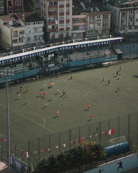 Aerial view of a soccer match in an urban stadium with colorful uniforms and a residential backdrop.