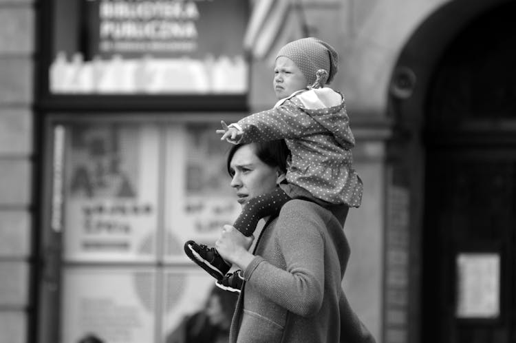 A Woman Carrying A Child On Her Shoulders