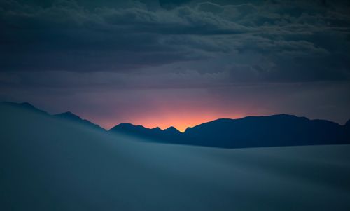 Free Scenic view of mountains silhouetted against a vivid sunset sky with clouds. Stock Photo
