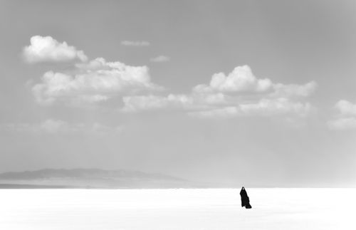 Free A lone woman in an abaya stands against a vast desert backdrop with clouds overhead. Stock Photo