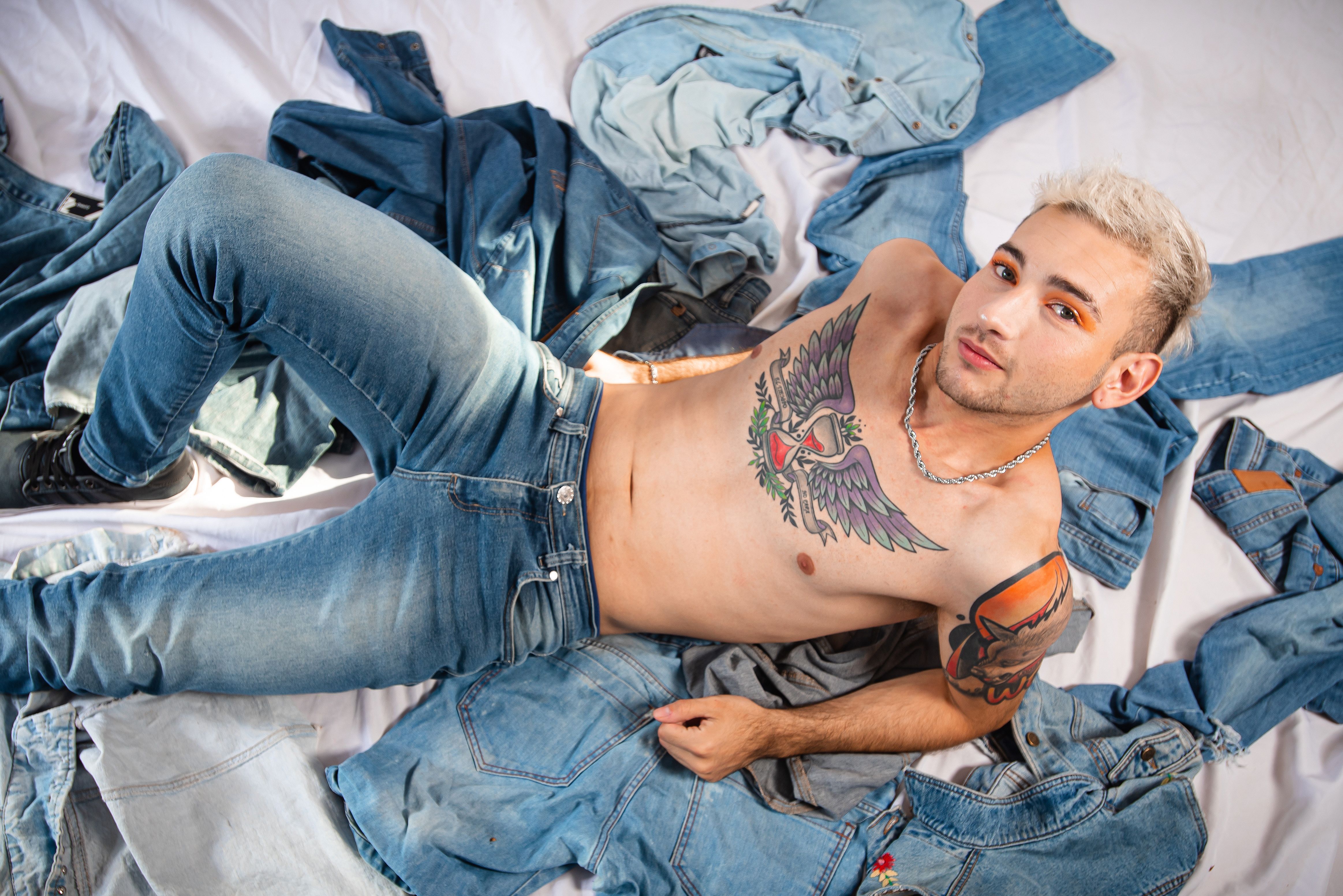A fashionable male model with tattoos lying on denim fabric in Argentina.