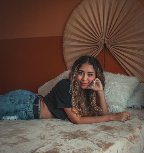 Free A young woman comfortably lying on a bed in a cozy, warmly decorated bedroom. Stock Photo