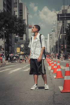 Young man in city street looking around, surrounded by buildings and traffic cones.