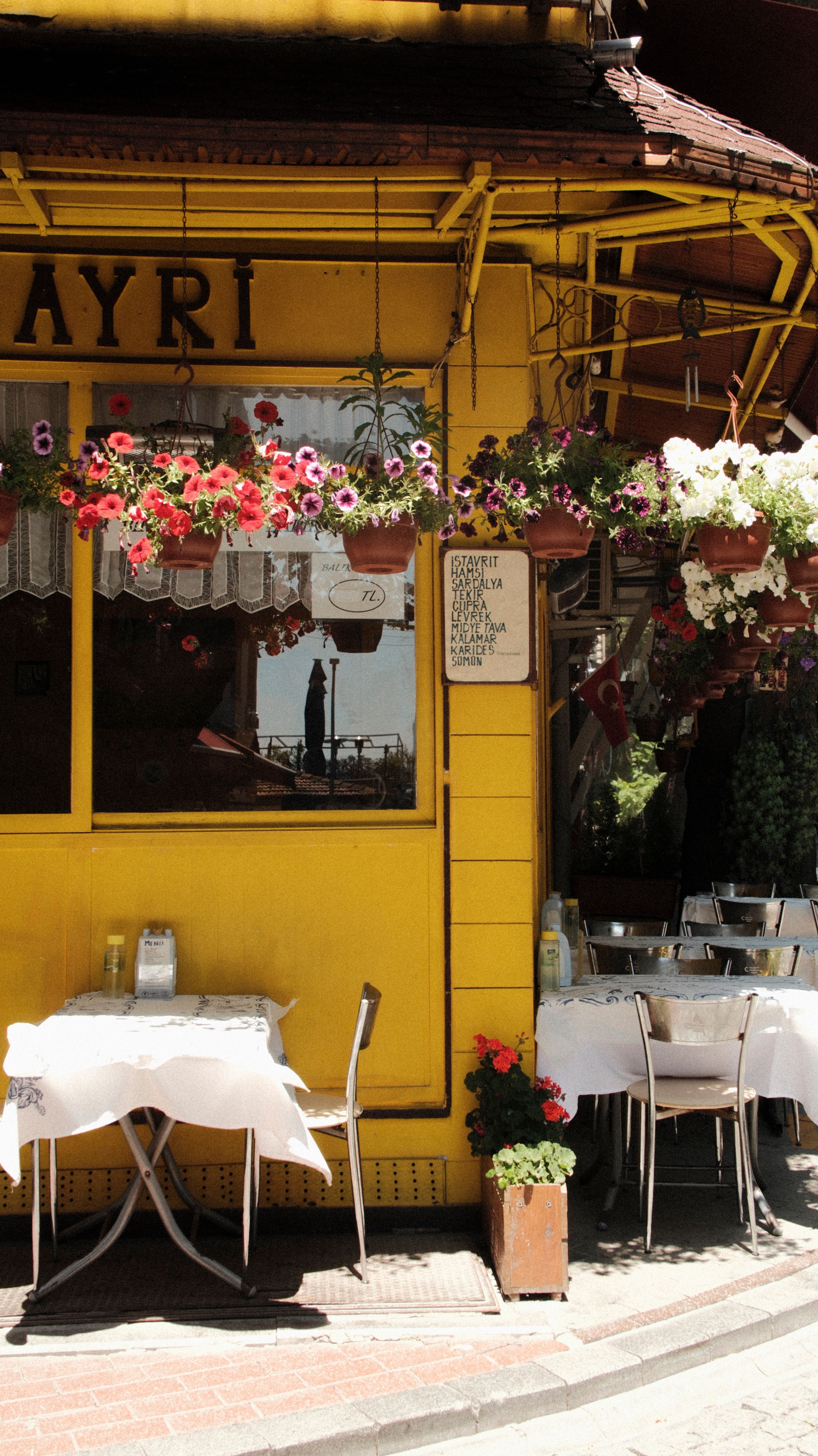 Quaint yellow café with flowers, tables, and sunlight creating an inviting atmosphere.