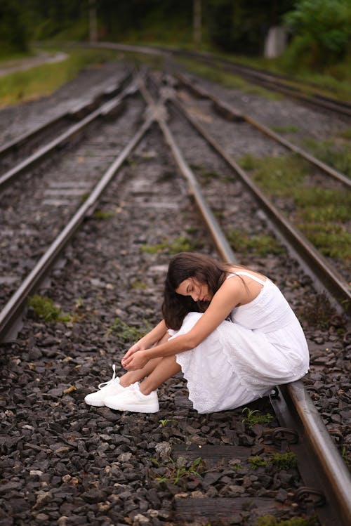 Young Woman in Dress Sitting on Railroad Tracks