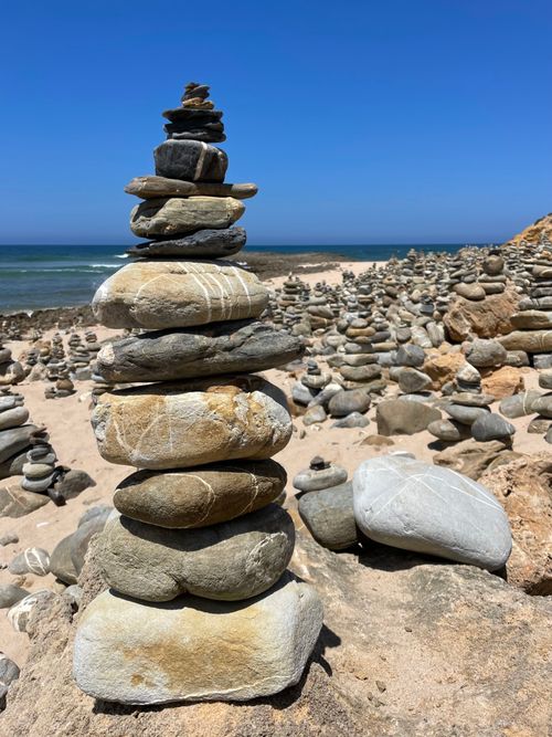 Free Close-up of balanced stones on a sandy beach under a clear blue sky. Stock Photo