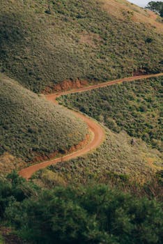 A scenic aerial view of a winding dirt road cutting through lush green hills.