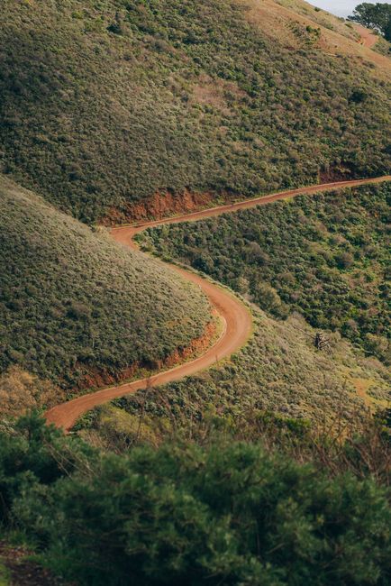 A scenic aerial view of a winding dirt road cutting through lush green hills.