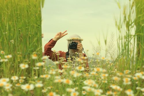 Free A woman in a flower meadow photographing while making a peace sign. Stock Photo
