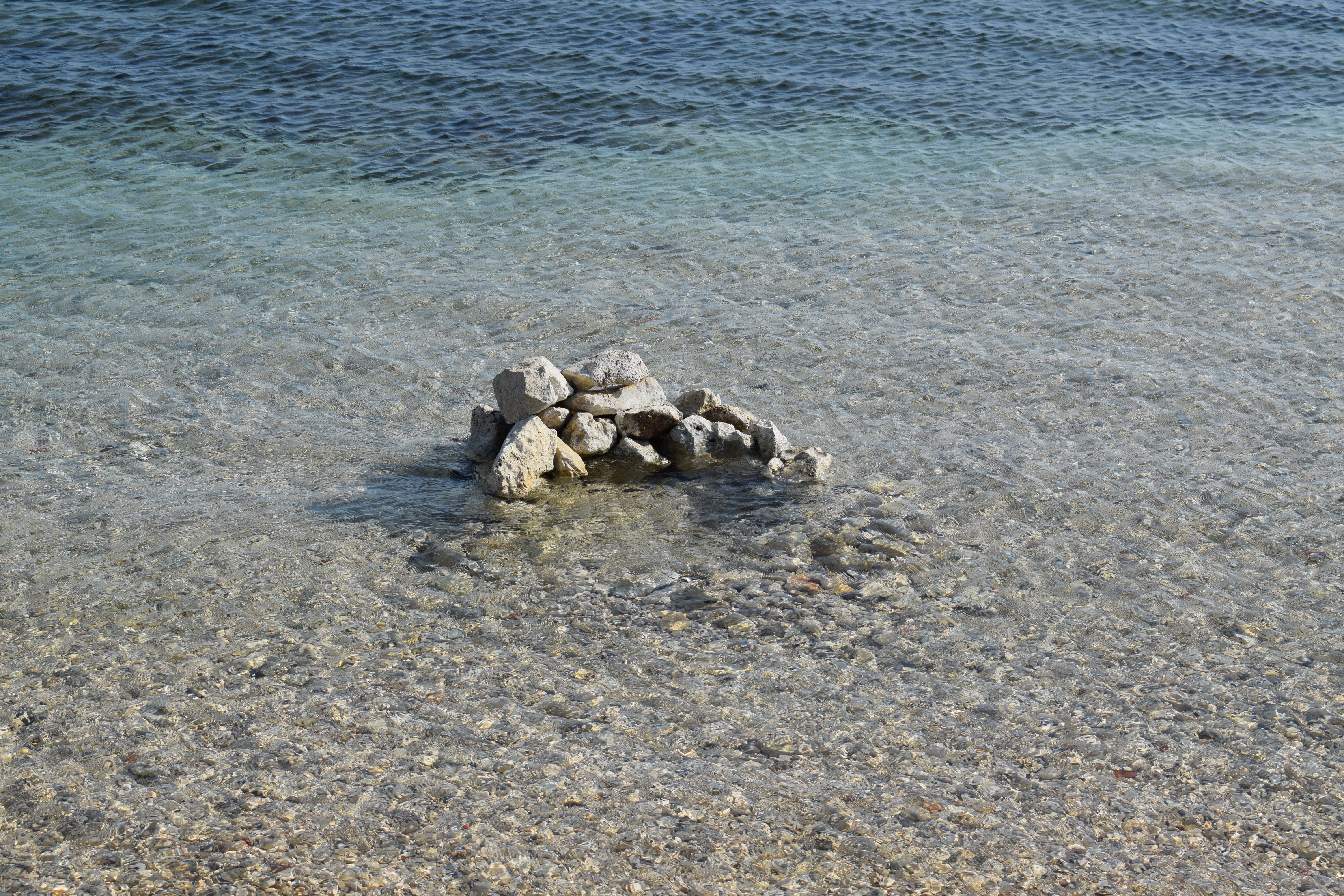 A tranquil ocean shore with stacked rocks reflecting on clear water, minimal wave action.