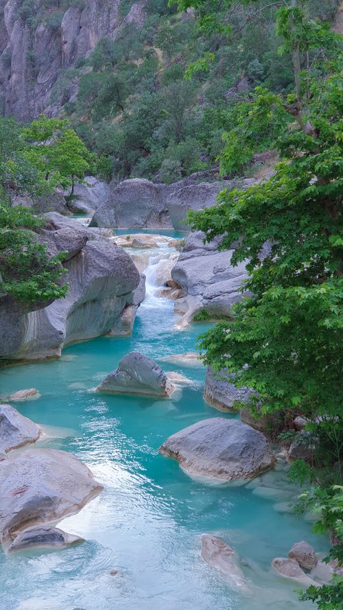 Free Crystal clear turquoise river flowing through lush, rocky canyon with vibrant greenery and rugged landscape. Stock Photo