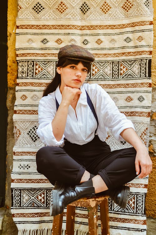 Young Woman in an Elegant Outfit Sitting on a Chair on the Background of a Fabric with Traditional Pattern 