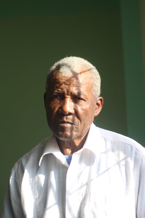 Portrait of an Elderly Man in a White Shirt Standing in Sunlight