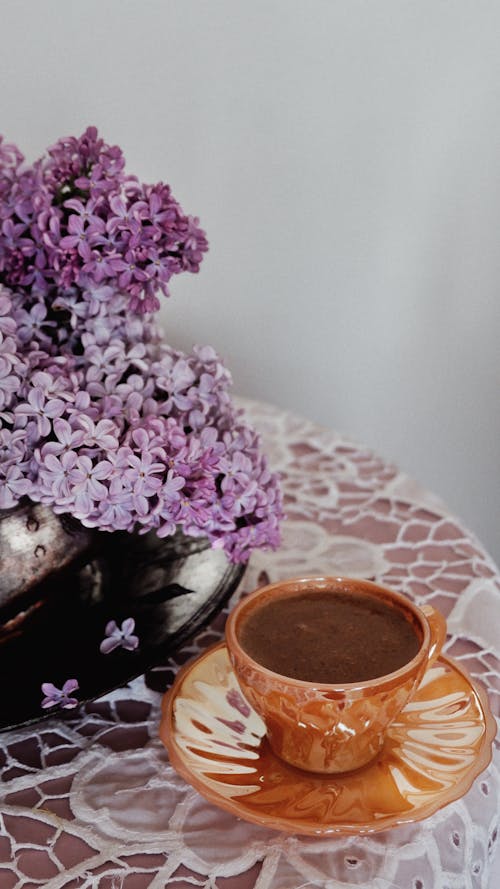 A Cup of Coffee and a Vase with Lilac Standing on the Table 