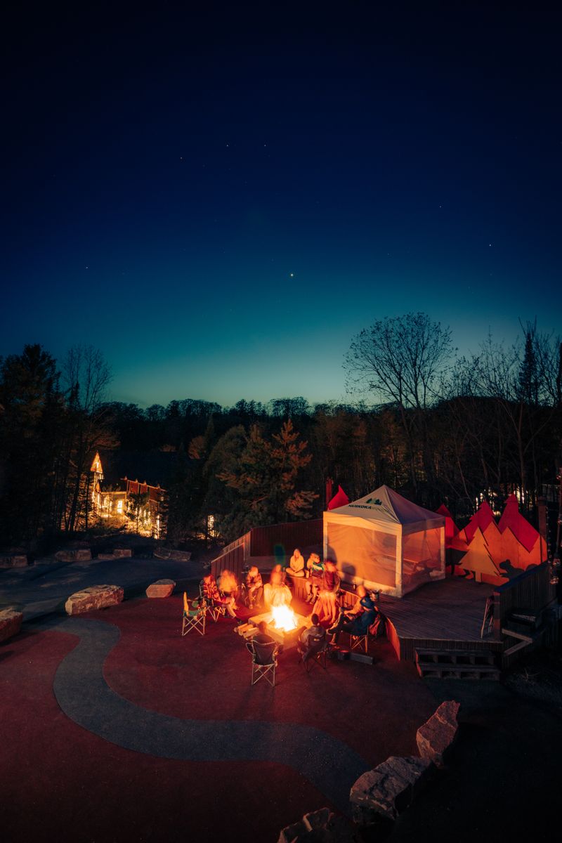 A lively campfire scene with friends at an outdoor campsite during twilight.