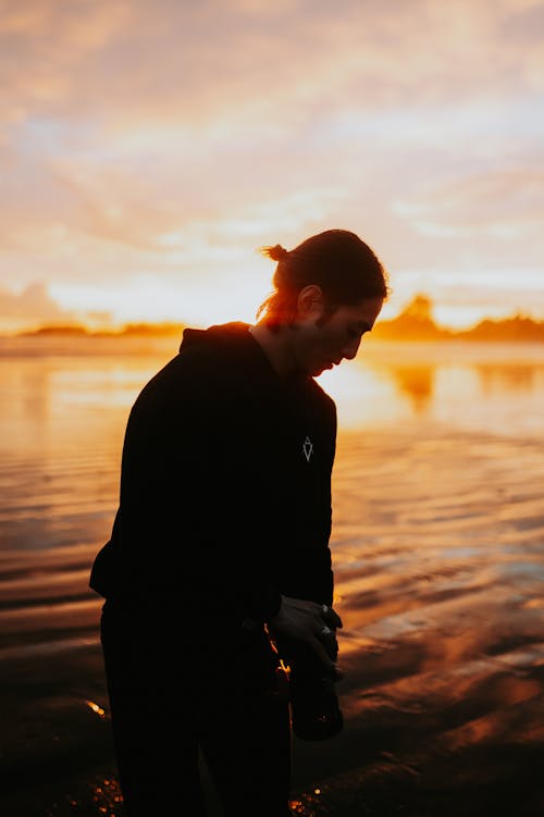 Young Man Standing by the Body of Water at Sunset 