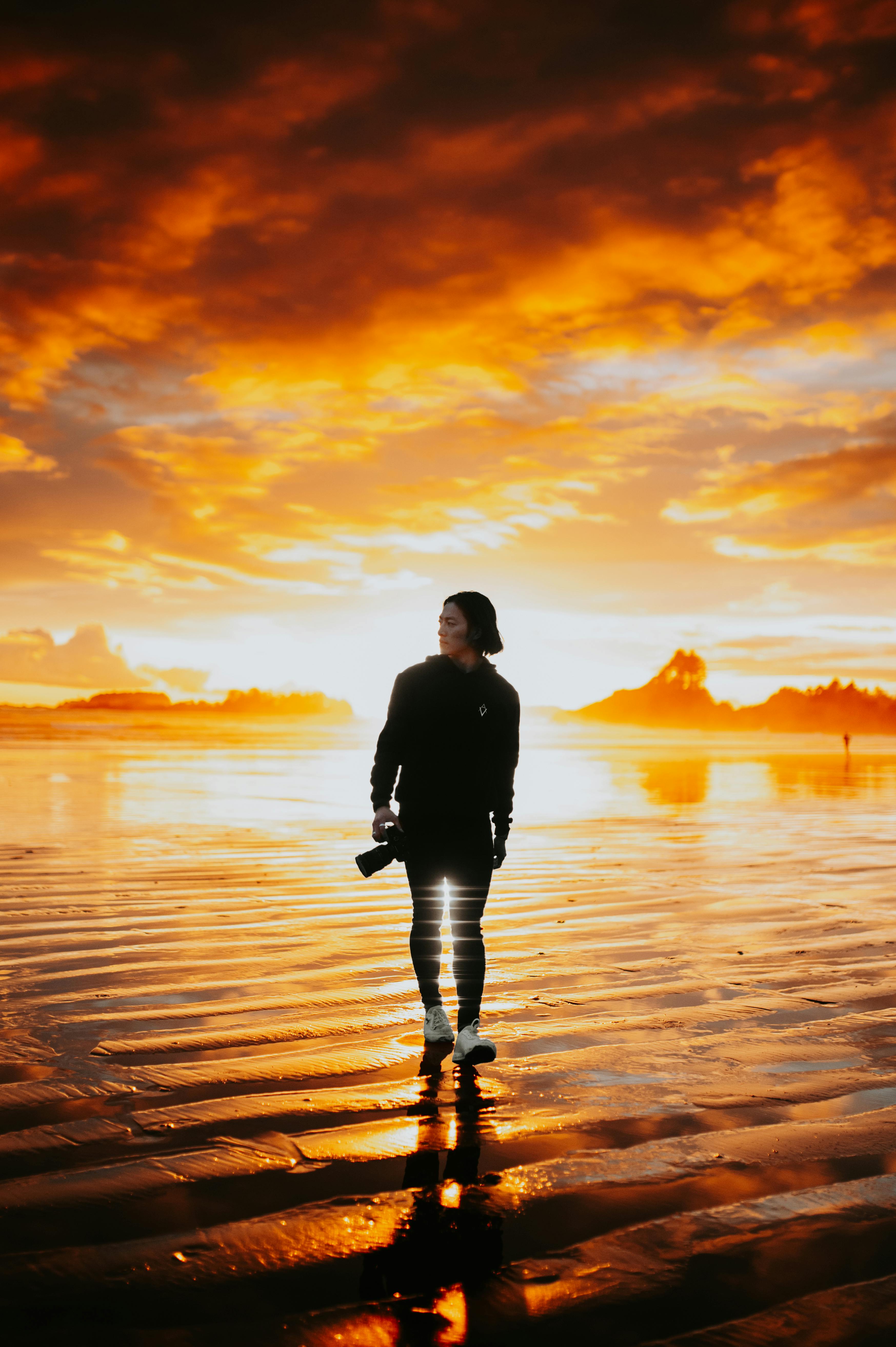 Captivating silhouette of a photographer walking along a beach during a dramatic sunset.