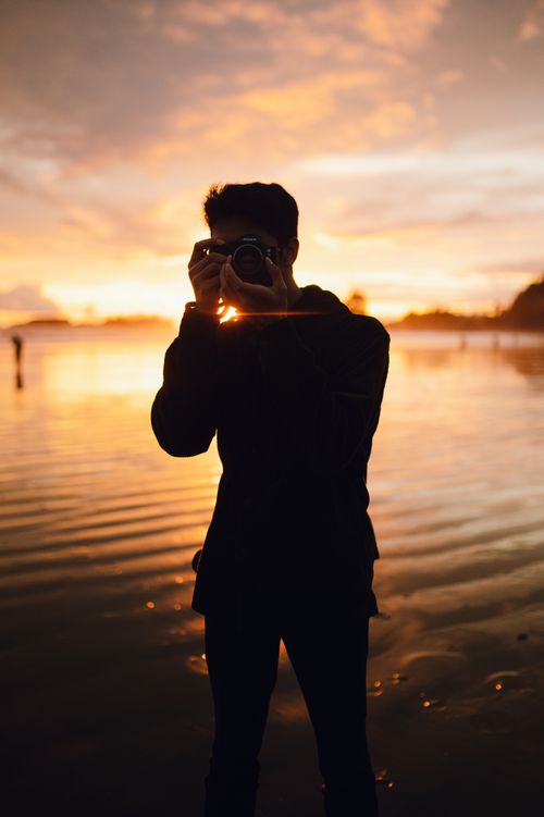Free Captivating silhouette of a photographer capturing a serene sunset by the lake shore. Stock Photo