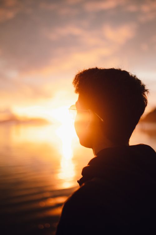 Free A young man enjoying a tranquil beach sunset, capturing warmth and reflection. Stock Photo