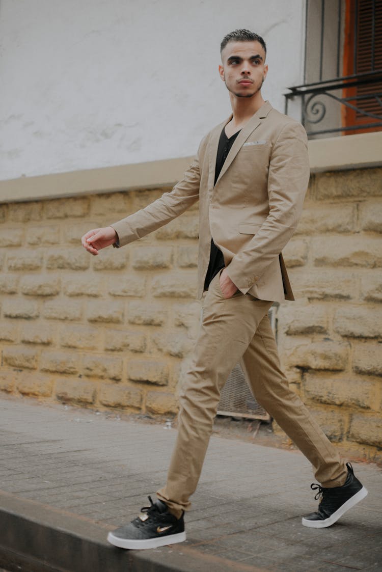 Young Man In A Beige Suit And Sneakers Walking On The Pavement 