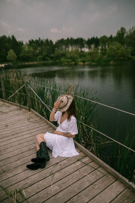 Woman in white dress sitting on a bridge by the lake, enjoying a serene summer day.