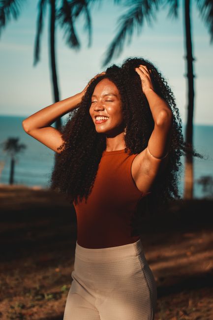 Portrait of a smiling woman with long curly hair enjoying the sun outdoors.