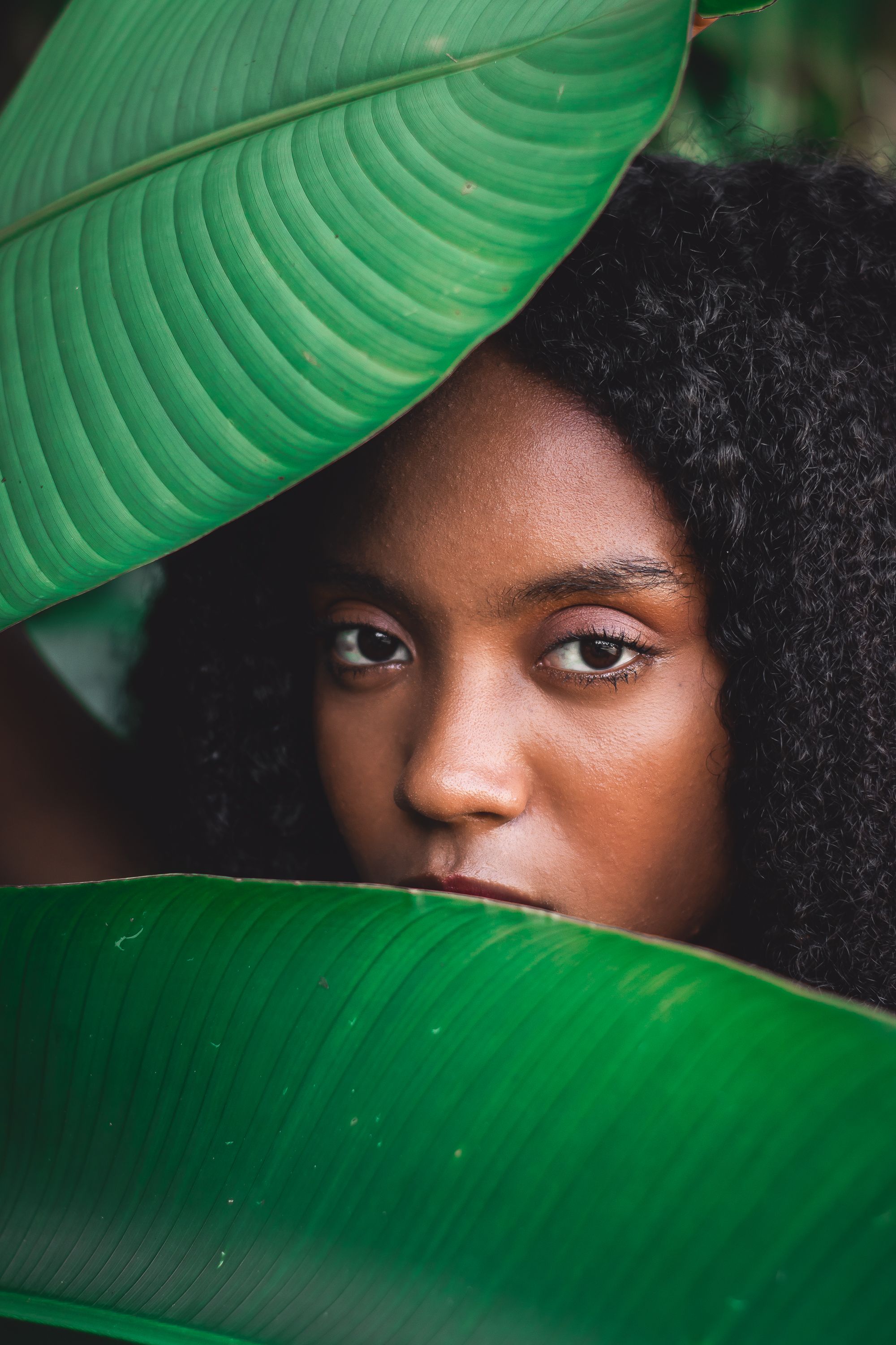 Attractive ethnic woman looking at camera through green plant