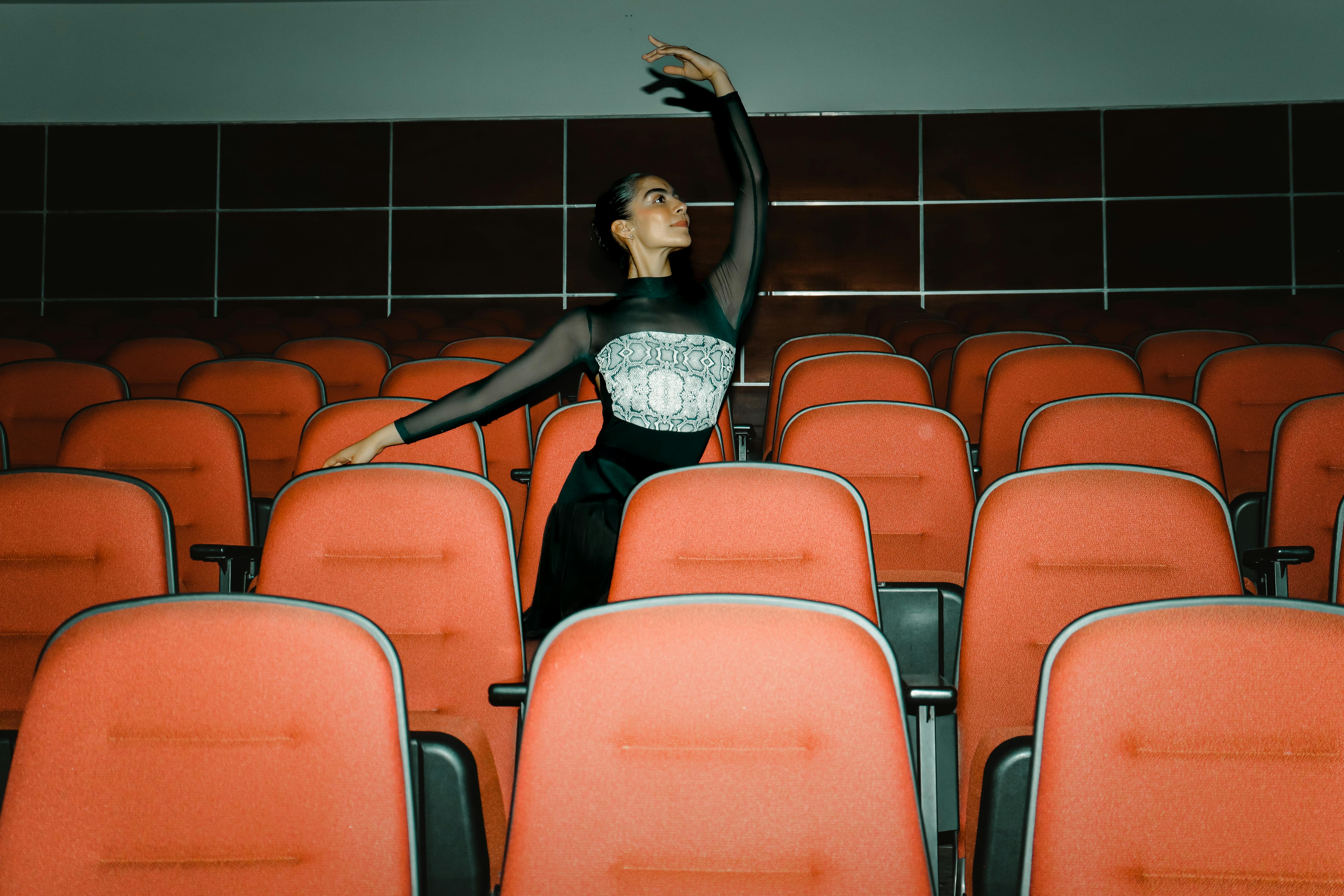 Free Elegant ballerina in a theater performing gracefully, surrounded by empty red seats. Stock Photo