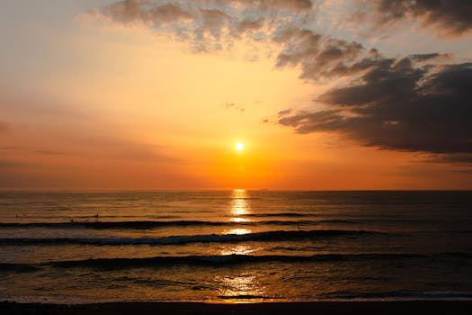Breathtaking sunset over the ocean with waves lapping at the shore and vibrant orange skies.
