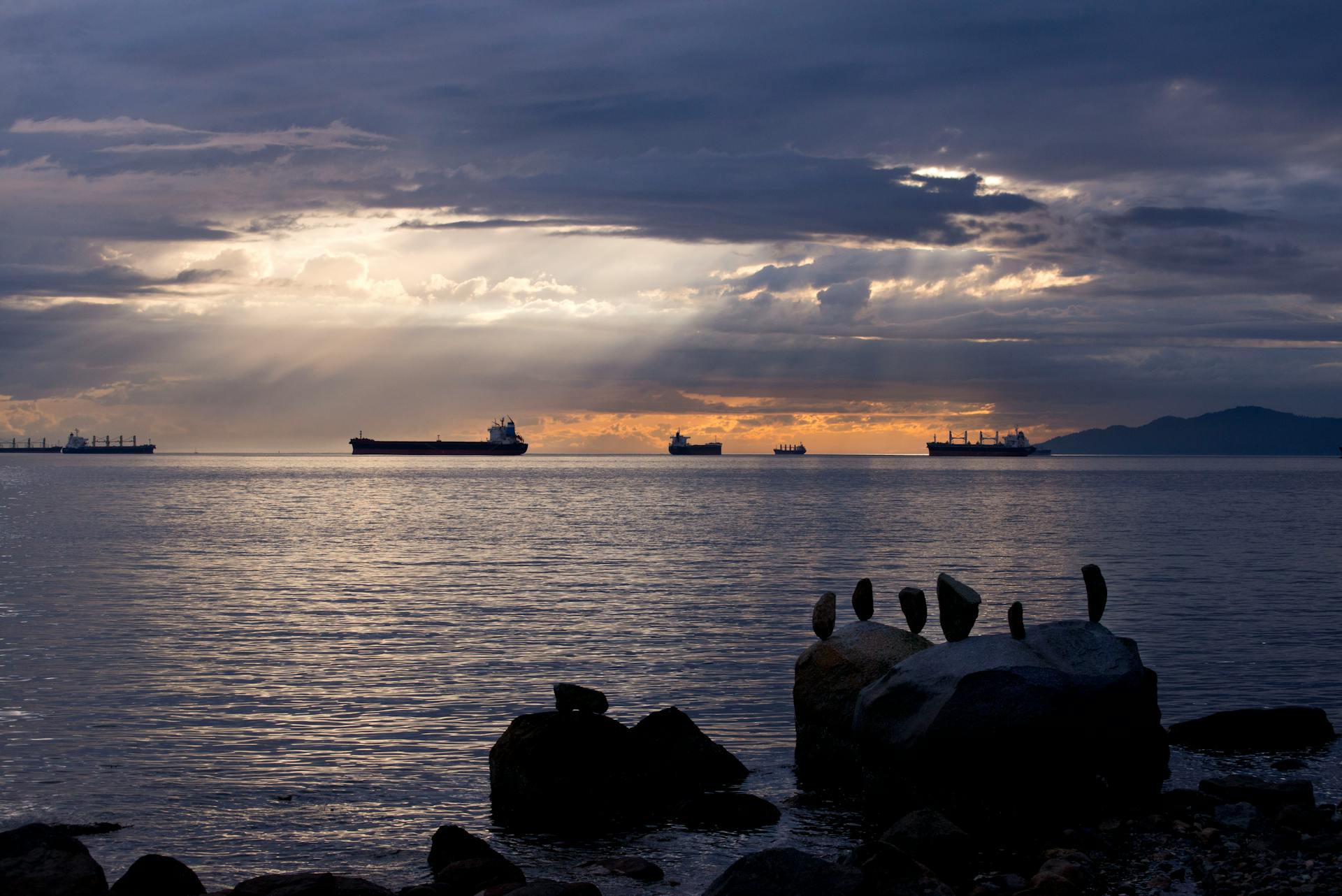 Peaceful ocean scene during sunset with silhouetted cargo ships and dramatic clouds.