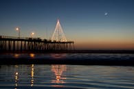 黄昏时分，平静的海面上倒映着码头明亮的灯光和月亮