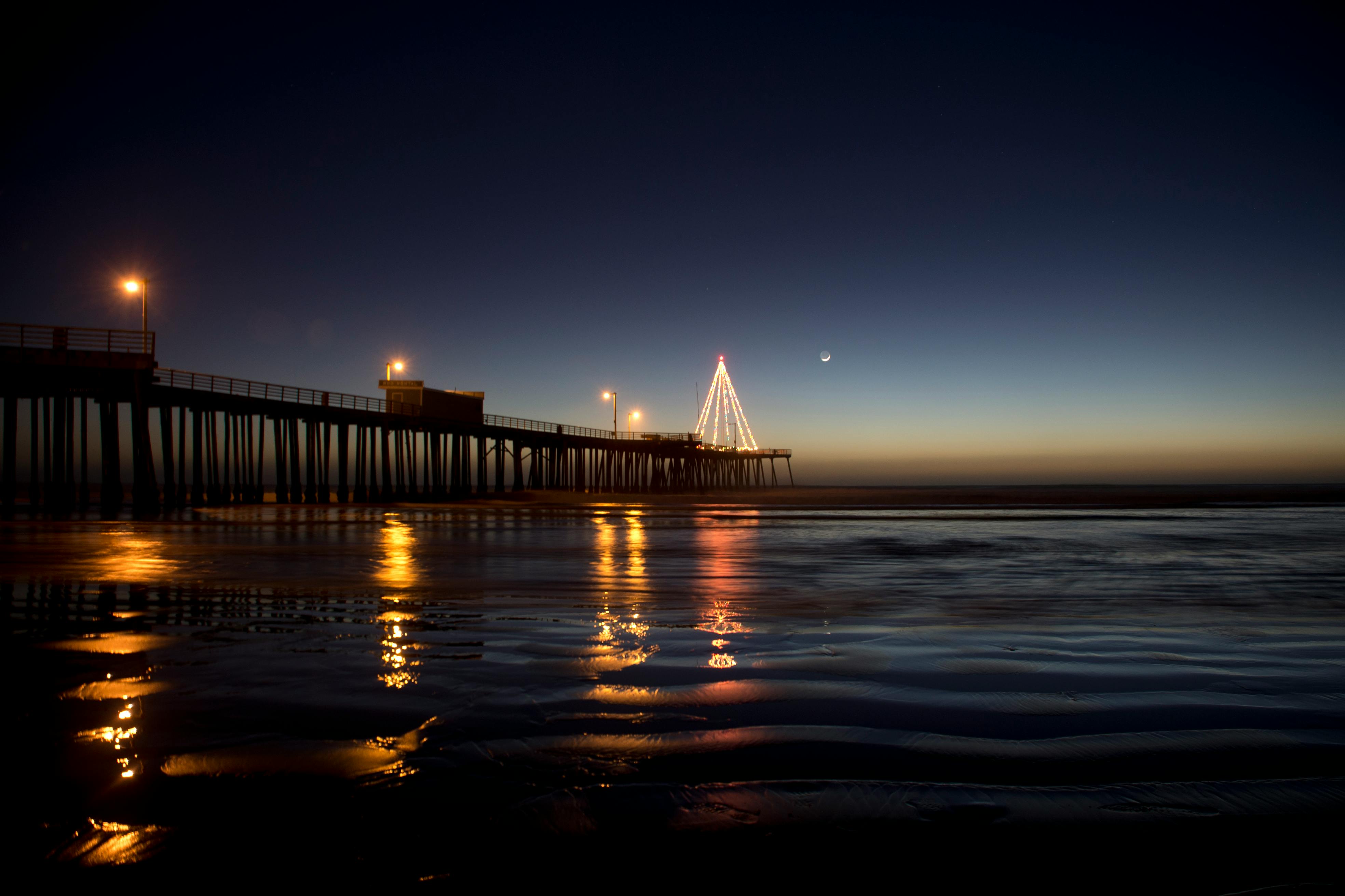 迷人的夜晚，码头现场点燃的灯光映照着平静的海水与上方的新月