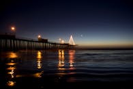 迷人的夜晚，码头现场点燃的灯光映照着平静的海水与上方的新月