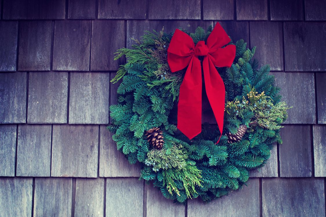 Finished DIY Christmas wreath with a red bow and pinecones hanging on a wooden wall