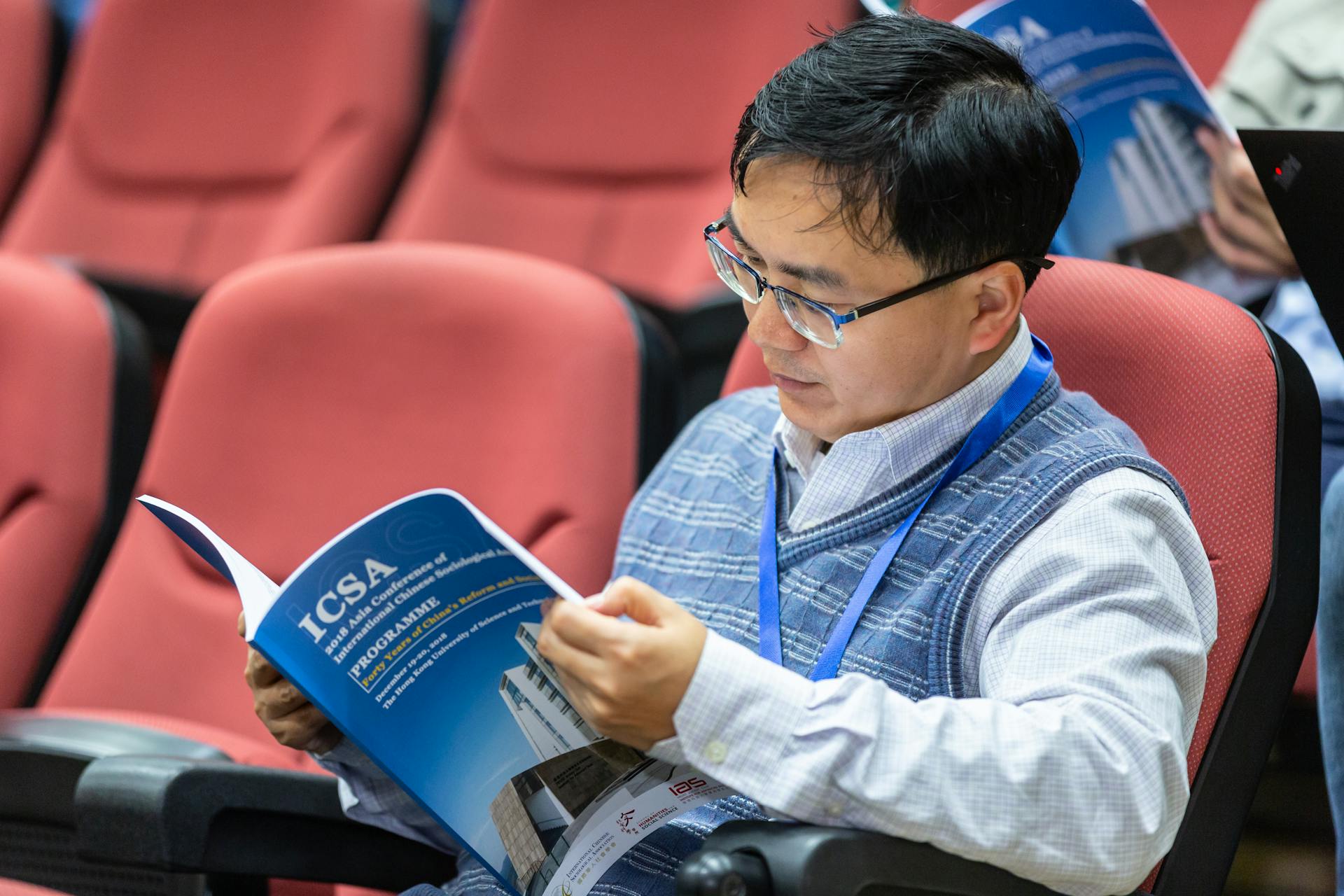 Adult man reading a conference program in an auditorium setting.