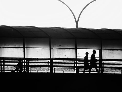 Free Black and white image of silhouettes walking through a glass-covered urban walkway. Stock Photo