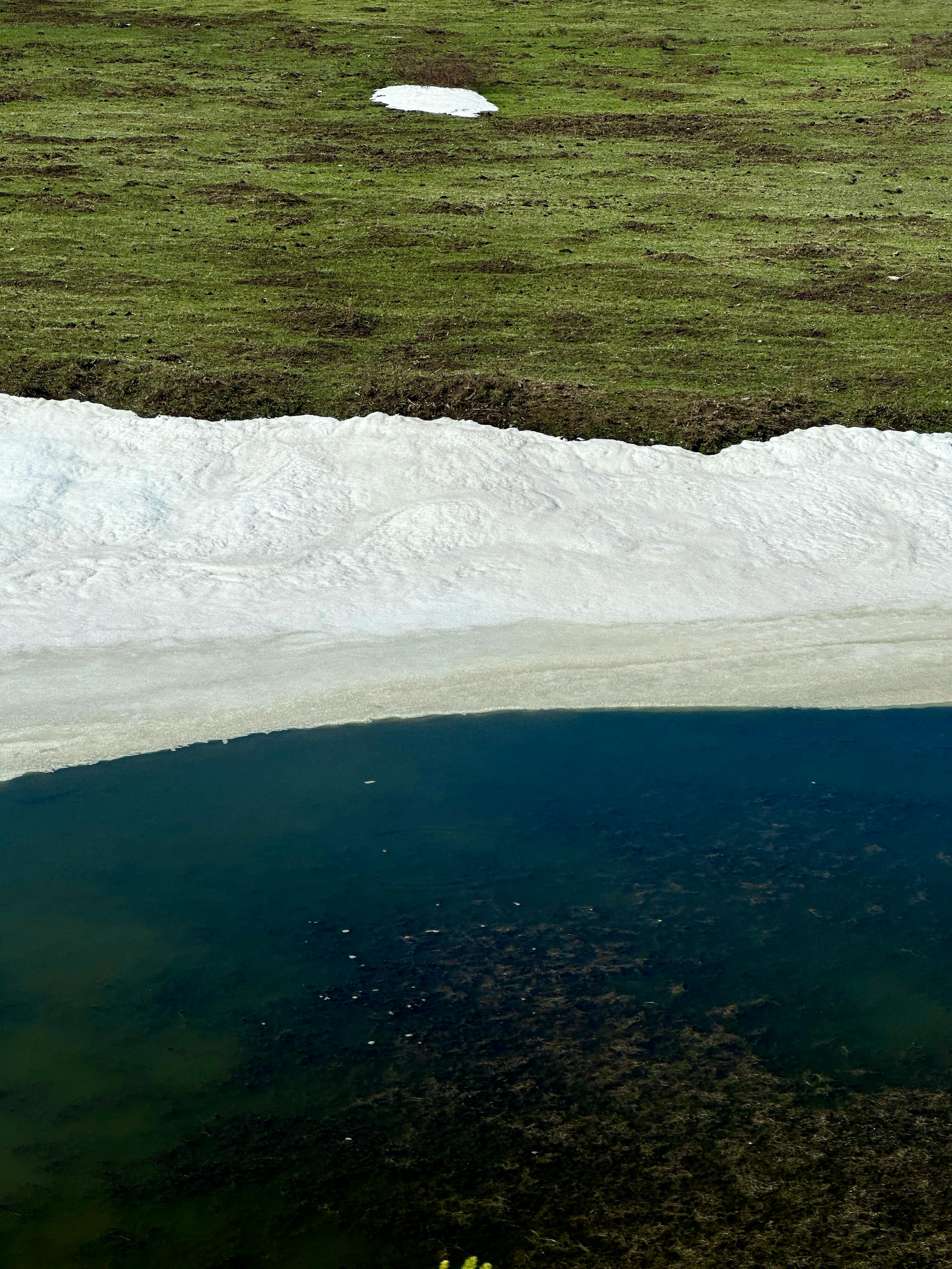 Peaceful lakeshore scene with green grass and melting snow.