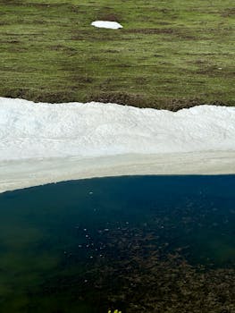 Peaceful lakeshore scene with green grass and melting snow.