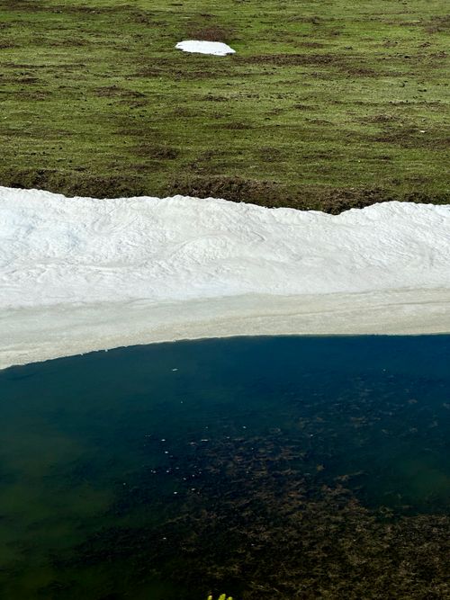 Free Peaceful lakeshore scene with green grass and melting snow. Stock Photo