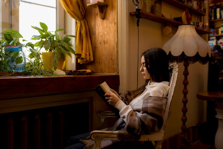 Young Woman Sitting Reading A Book In A Cozy Room