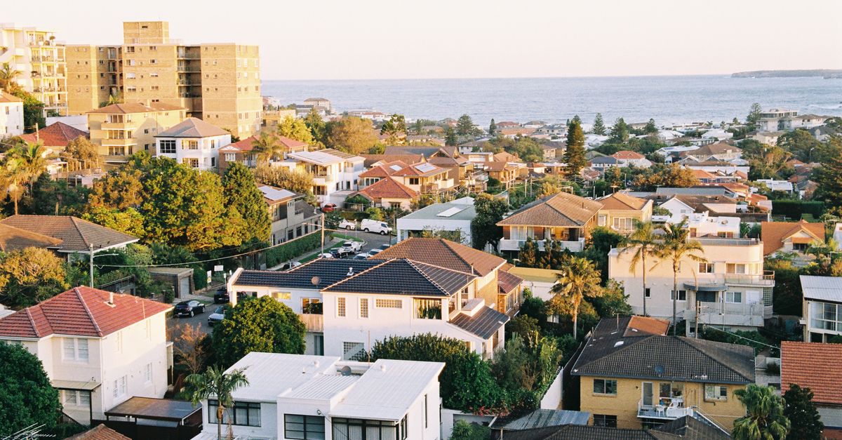 Aerial view of a coastal town with colorful houses and sea horizon at sunset.