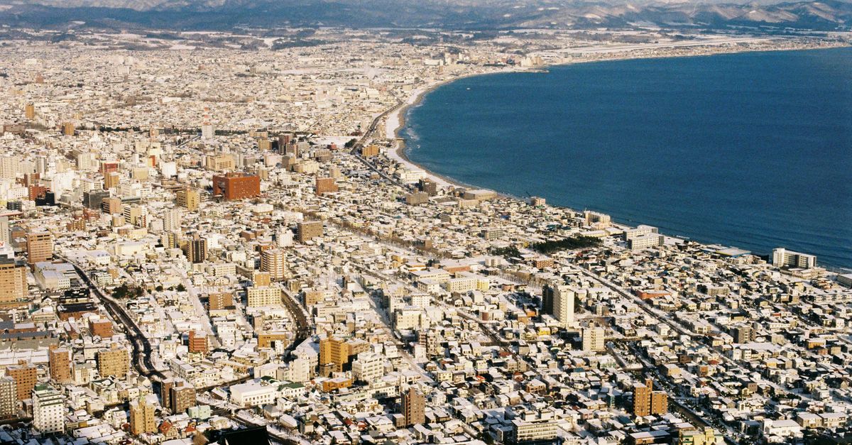 Stunning aerial view of a snow-covered coastal city meeting the blue sea during winter.