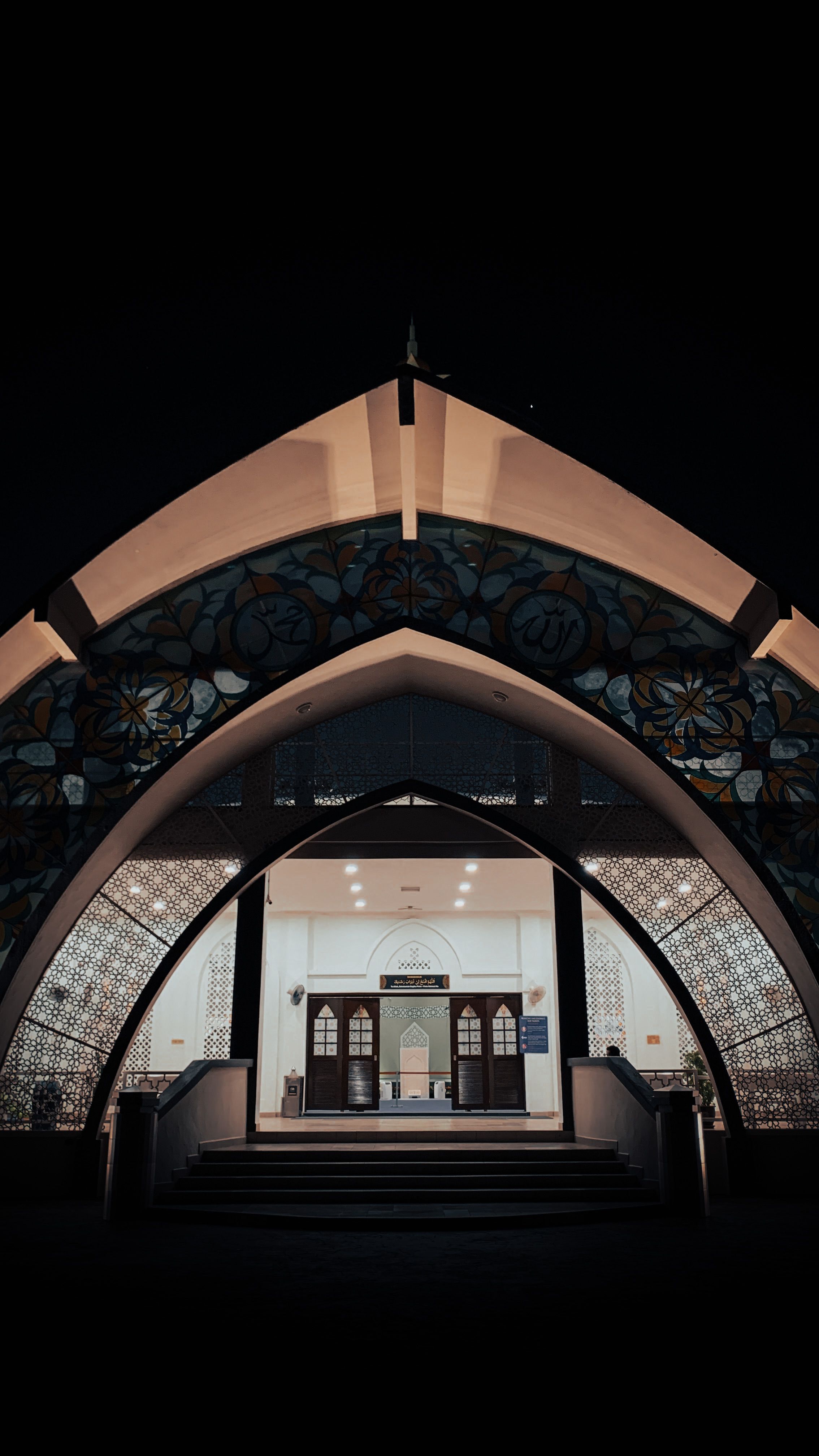 Stunning night view of an illuminated mosque entrance showcasing Islamic architecture in Melaka, Malaysia.